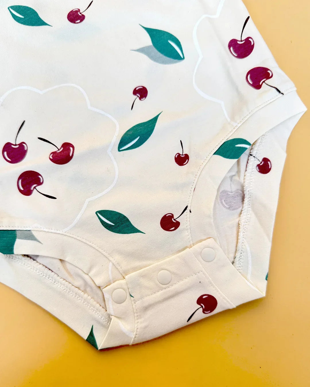 White baby onesie with cherry pattern on a yellow background