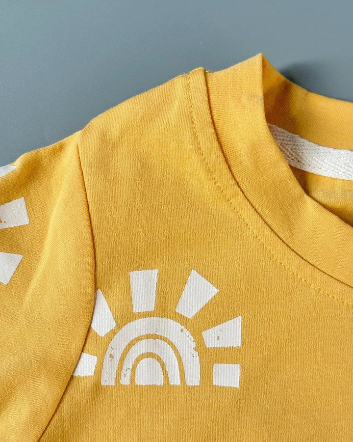 Yellow garment with a white sun and rainbow design on a gray background