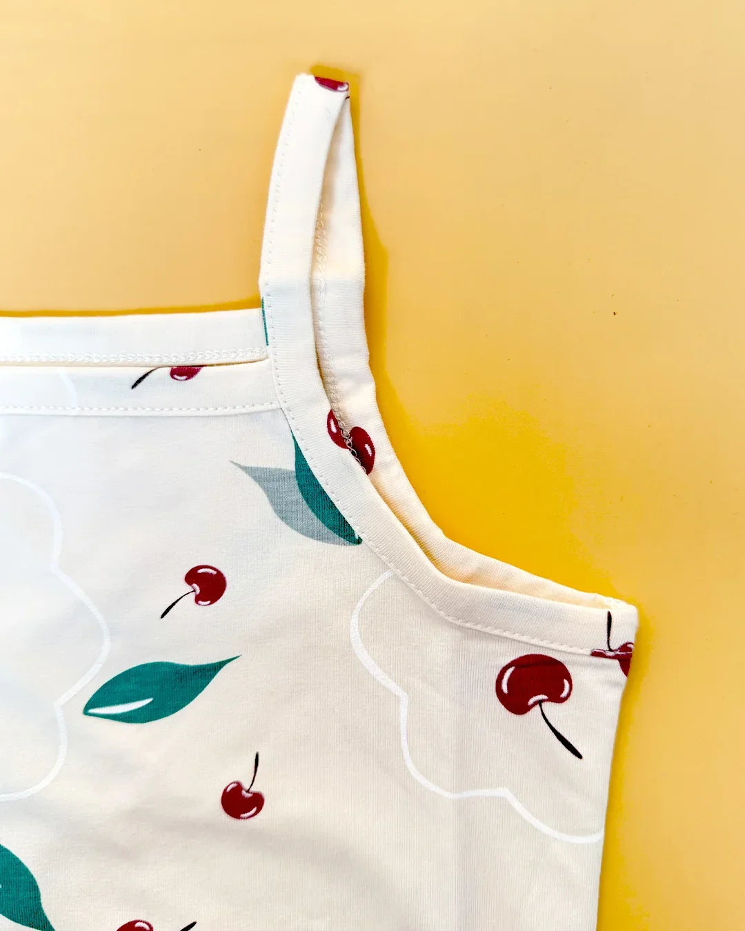 White apron with red cherry and green leaf pattern on a yellow background