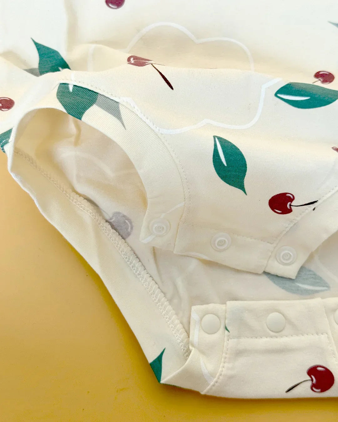 Baby onesie with cherry and leaf pattern on a yellow background