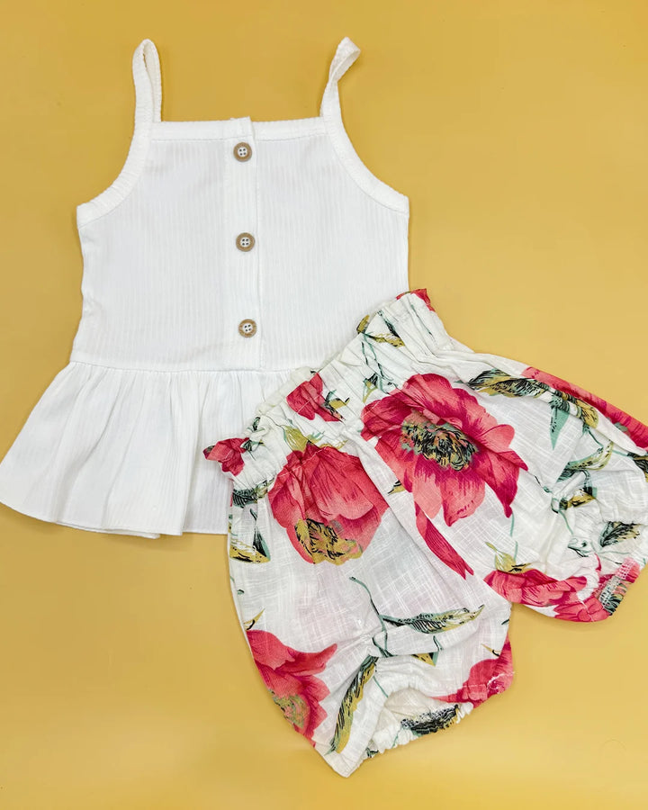 White sleeveless top with buttons and floral shorts on a yellow background