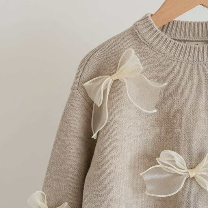 Beige sweater with white bow details on a neutral background