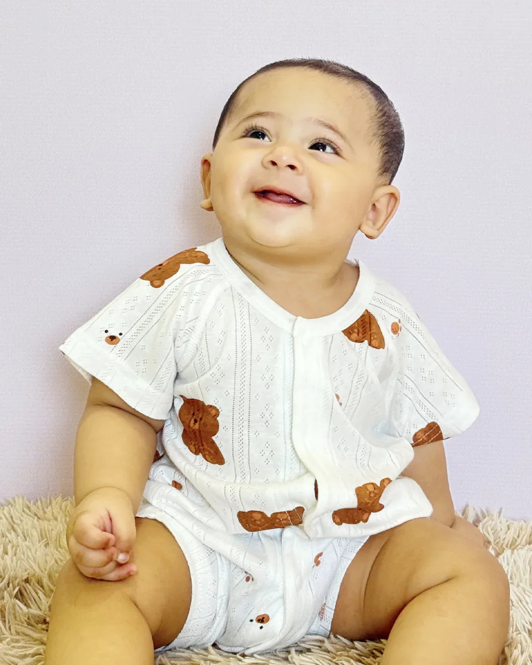 Baby wearing a white outfit with brown bear designs on a light purple background