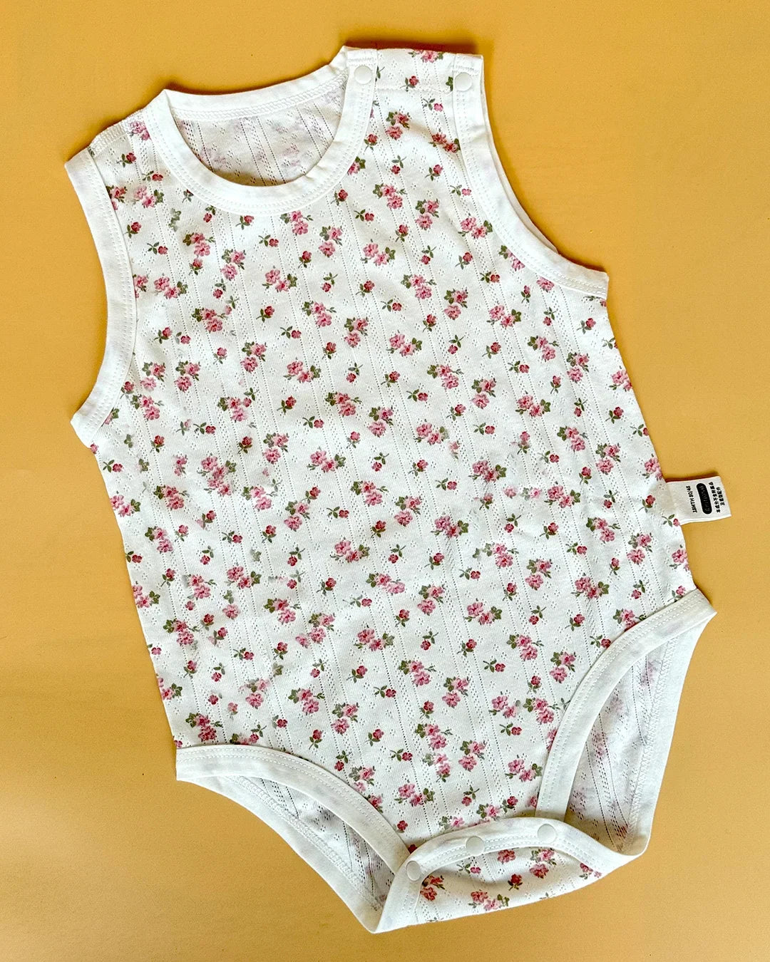 Floral-patterned baby onesie on a yellow background