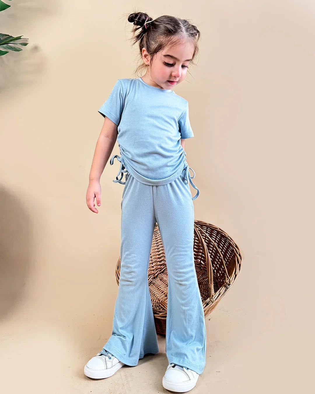 Child wearing a light blue outfit with wide-leg pants and a t-shirt, standing against a beige background.
