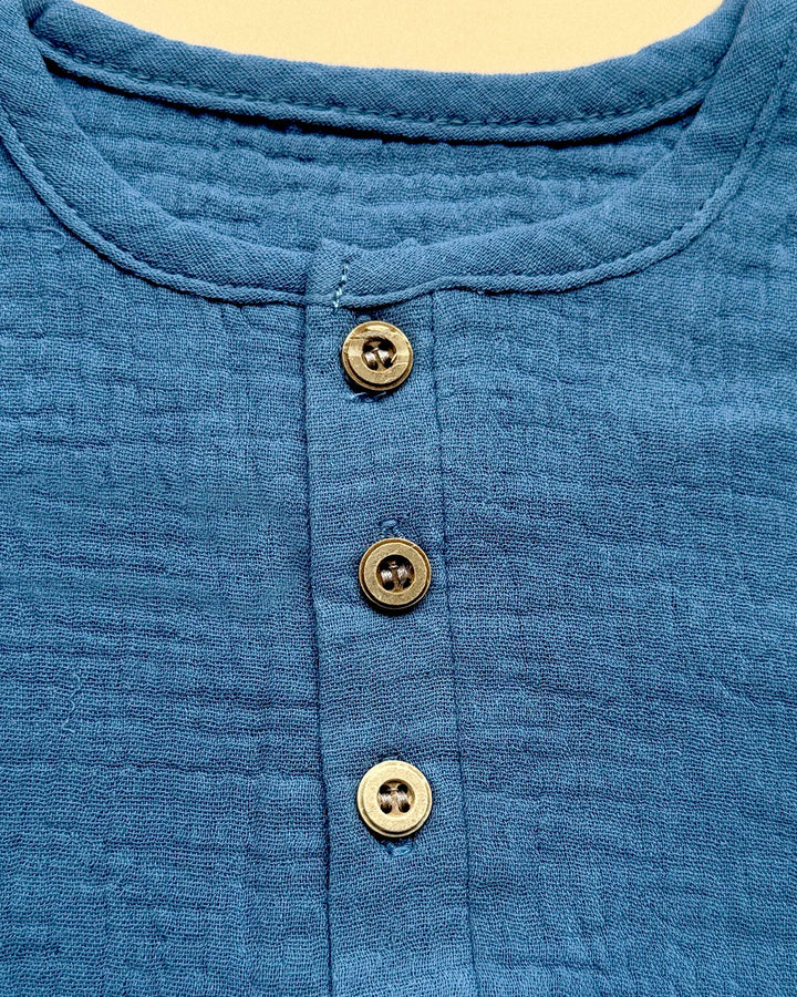 Close-up of a blue shirt with three brass buttons on a beige background