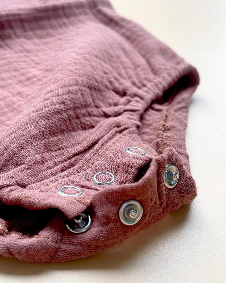 Close-up of a pink baby romper with button closures on a light background