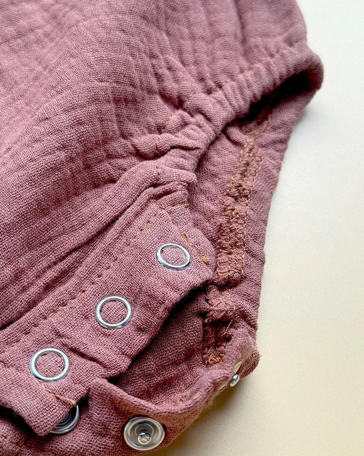Close-up of a pink baby romper with button details on a light background