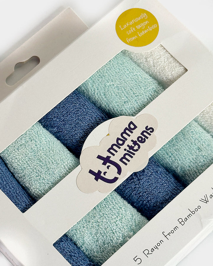 A set of five solid colored cotton baby washcloths in pastel blue and gray, packaged in a branded box with a label showing the brand name and the word 'Mittens'.