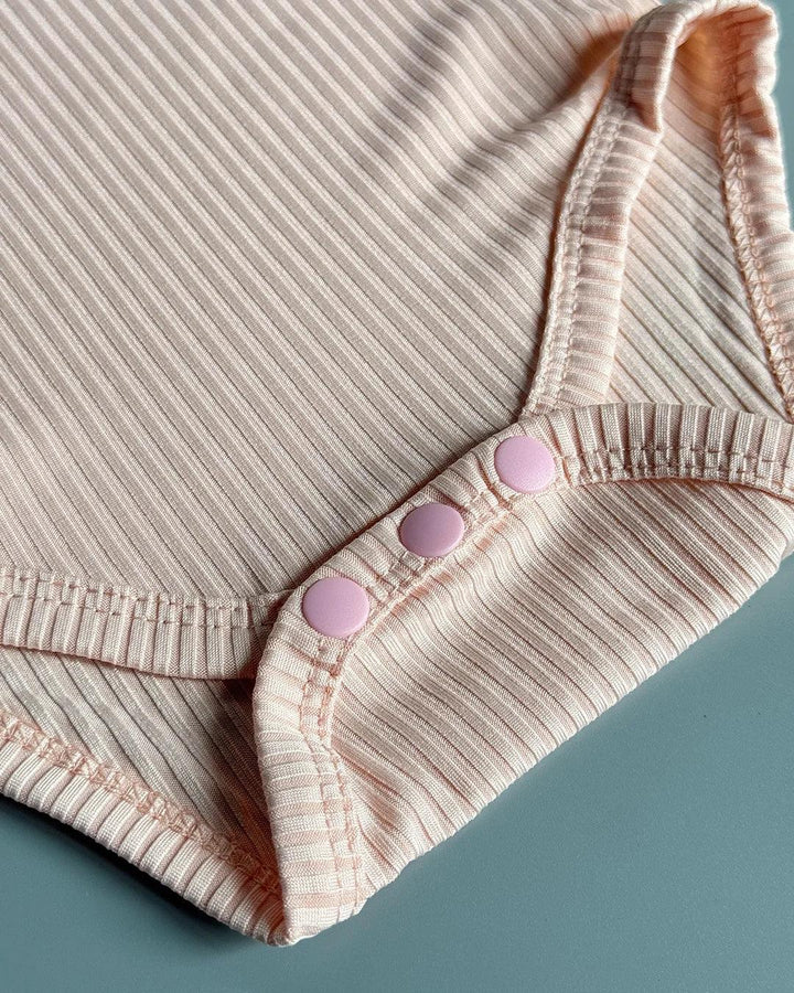 Close-up of a ribbed pink baby onesie with button details on a blue background