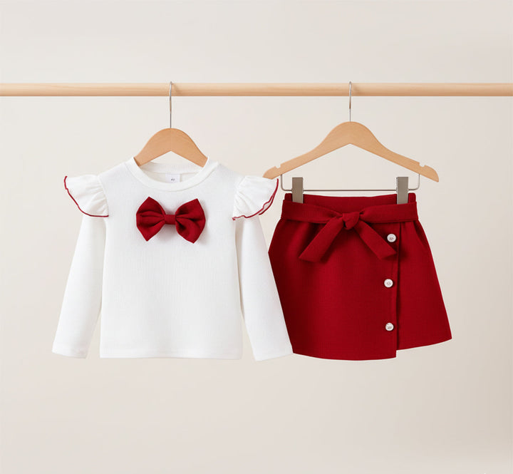 White blouse with red bow and red skirt with buttons on hangers against a beige background