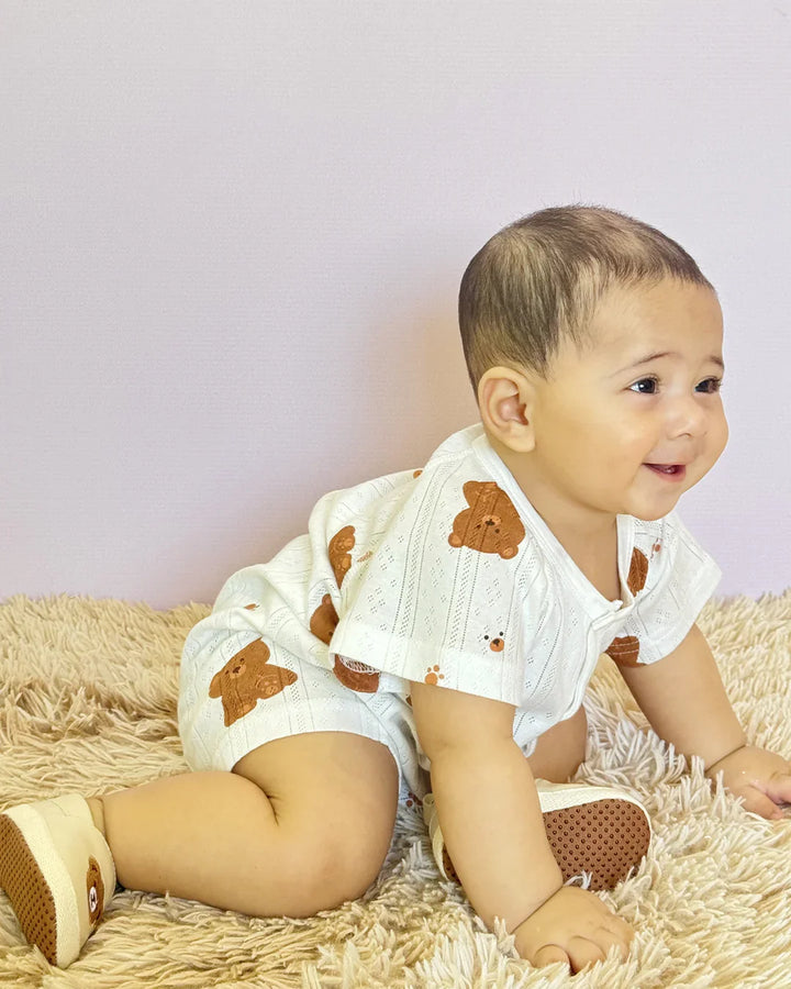 Baby wearing a white outfit with brown bear designs on a beige surface