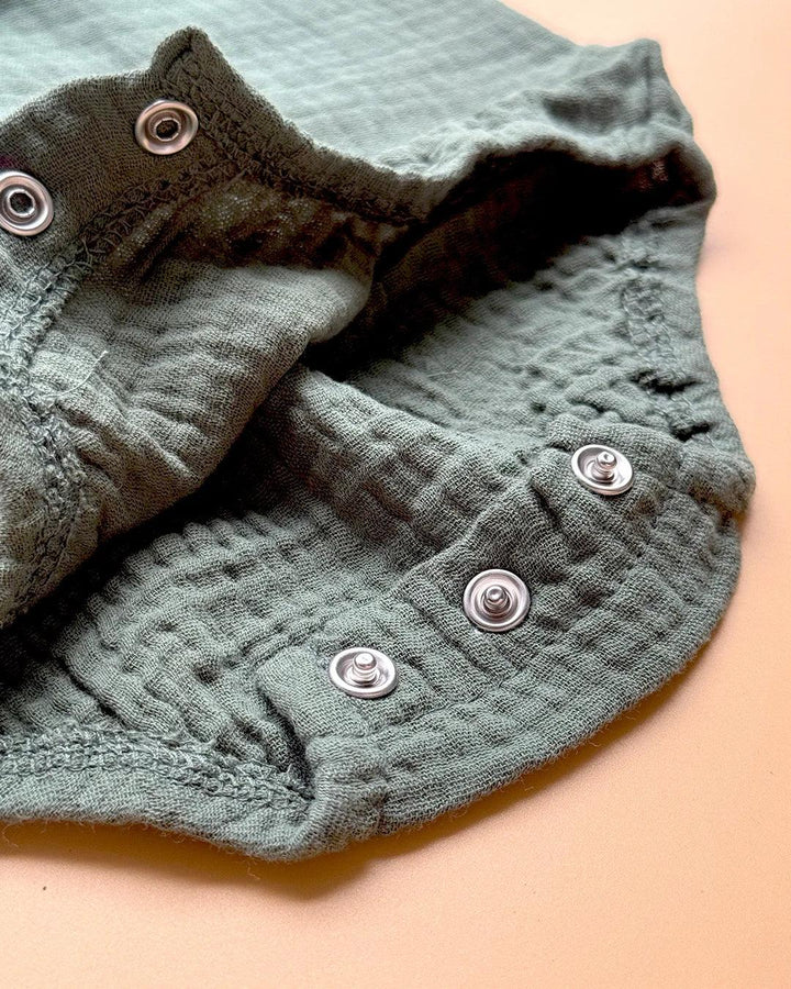 Close-up of a textured green baby outfit with buttons on a beige background