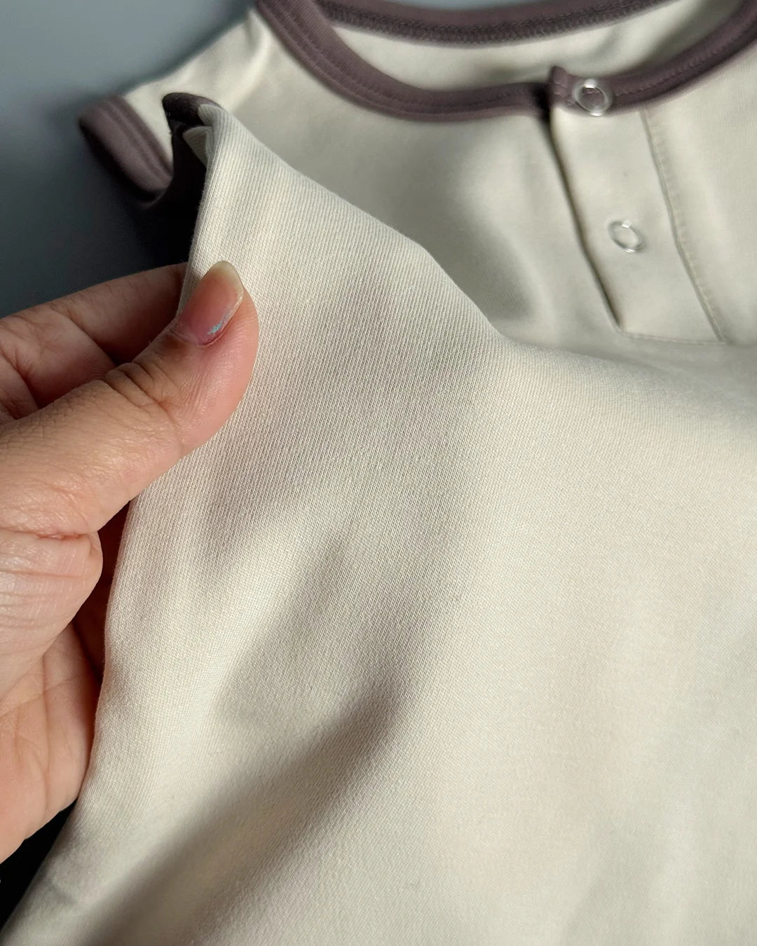 Close-up of a beige fabric with a hand holding it, against a neutral background.