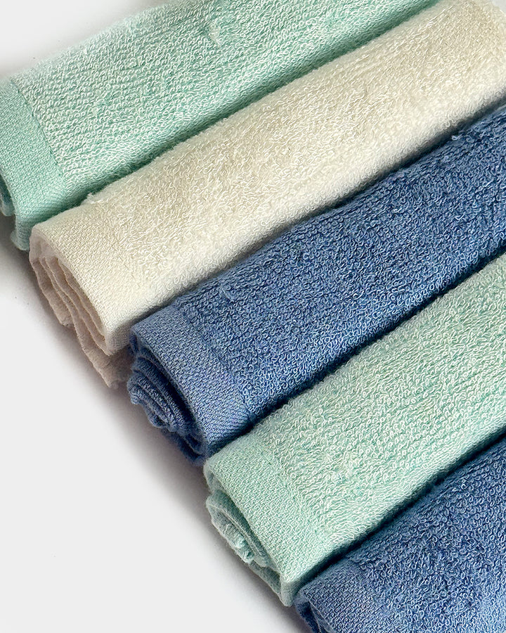 Folded towels in four colors: light green, beige, blue, and a mix of green and blue.