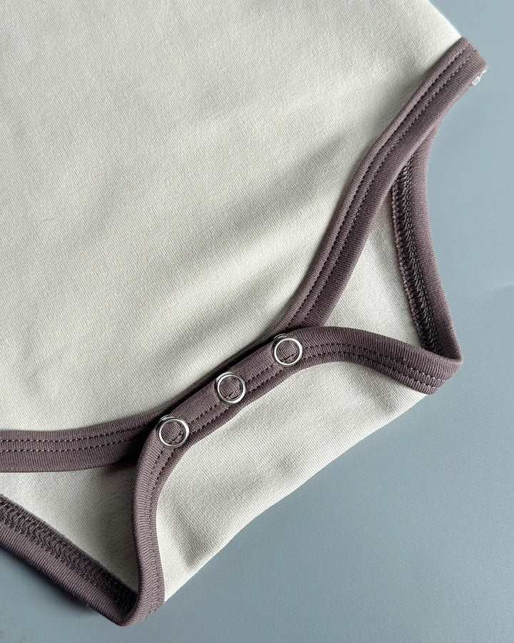 Close-up of a beige baby bodysuit with brown straps on a gray background