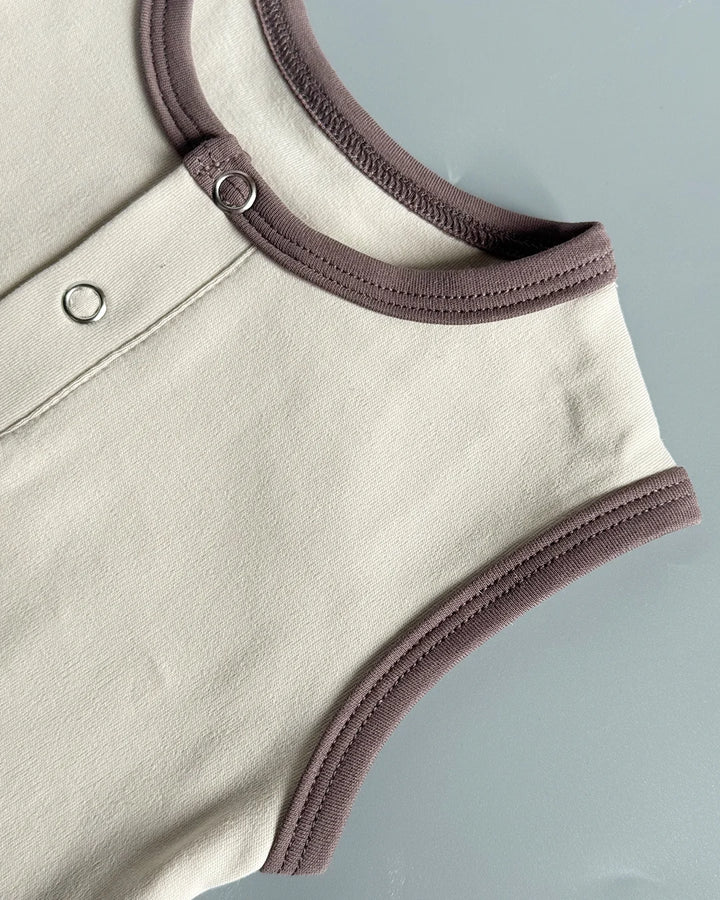 Close-up of a beige baby romper with brown trim on a light gray background