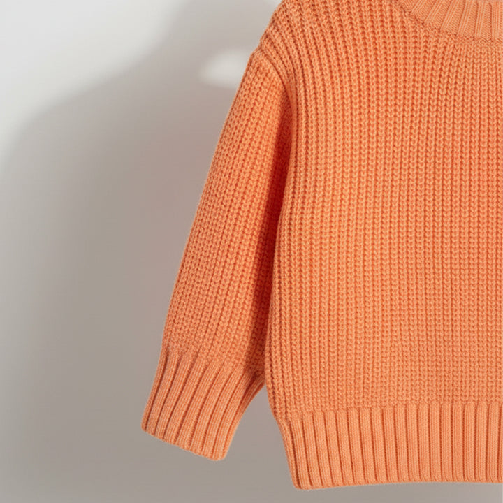 Close-up of an orange knitted sweater on a plain background
