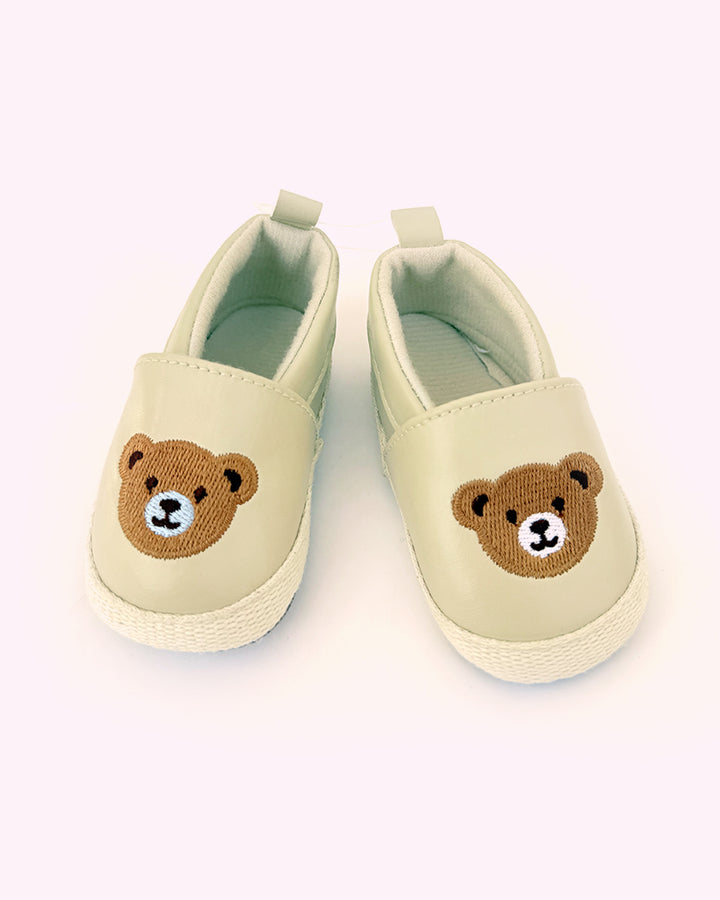A pair of beige slip-on style baby loafers with cute bear embroidery on the top.