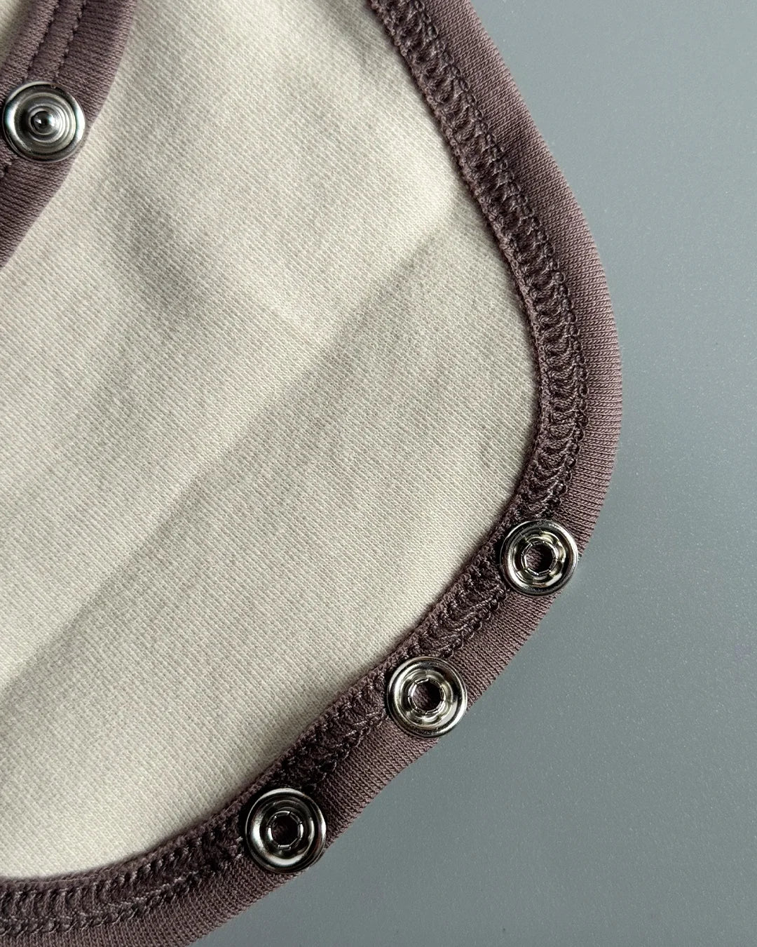 Close-up of a fabric product with brown trim and metal buttons on a gray background