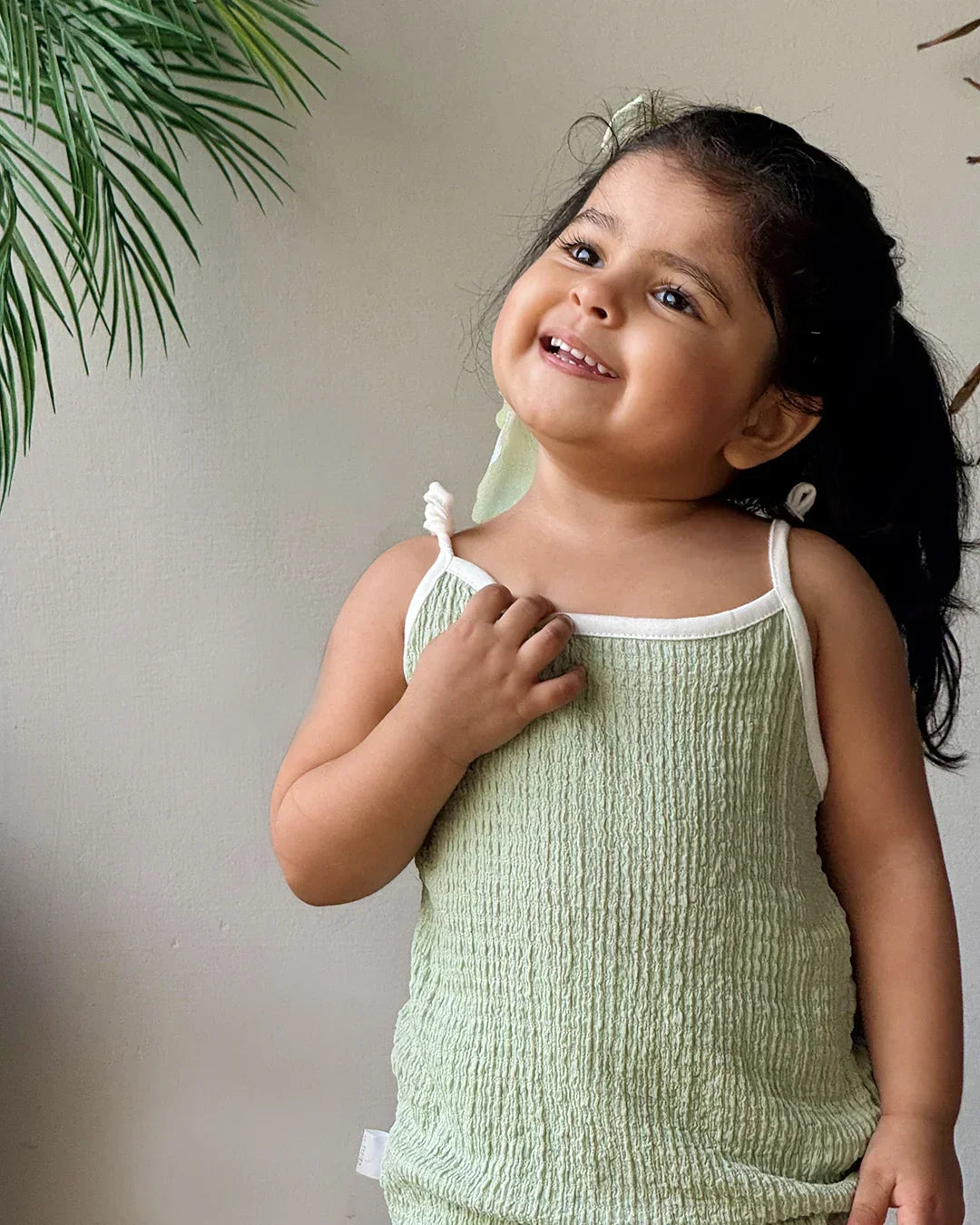 Child wearing a green sleeveless outfit with a white background
