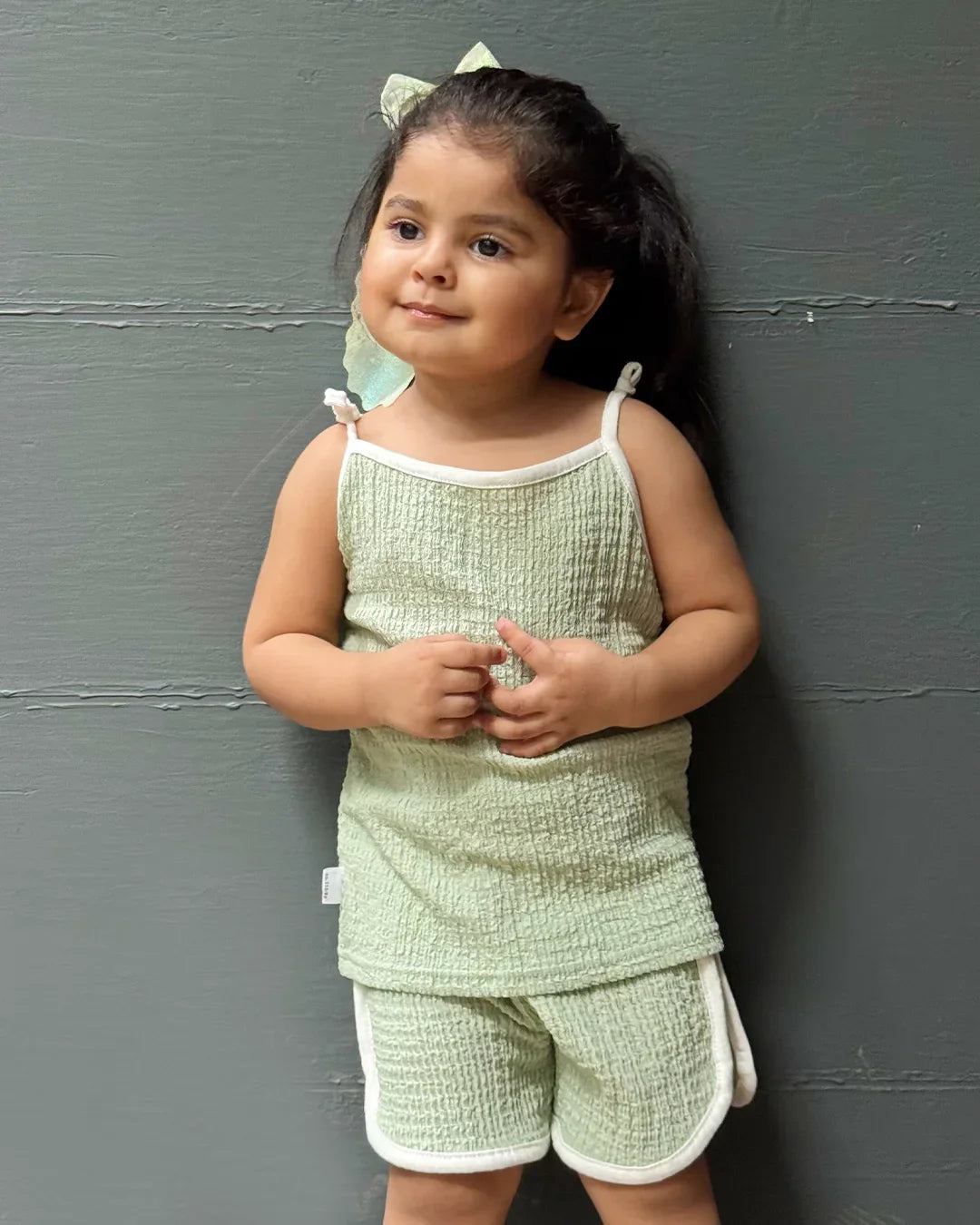 Young child wearing a light green textured outfit against a gray wall