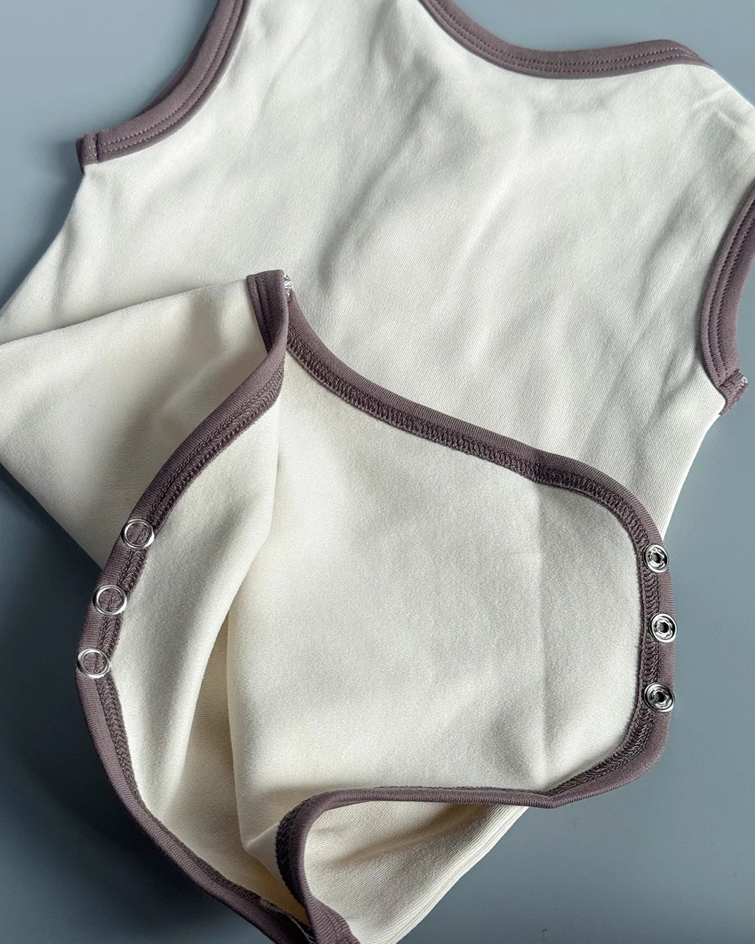 White baby bodysuit with brown trim on a gray background