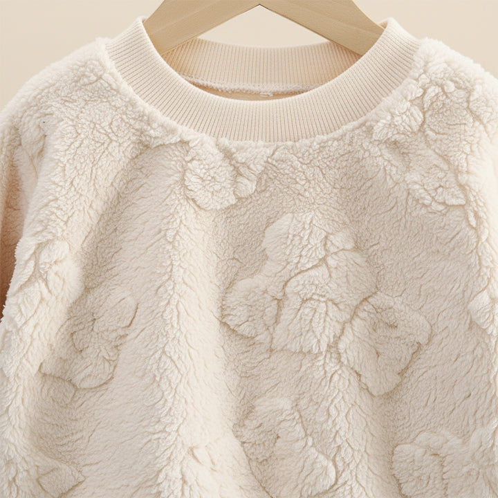 Close-up of a textured cream sweater on a hanger against a neutral background