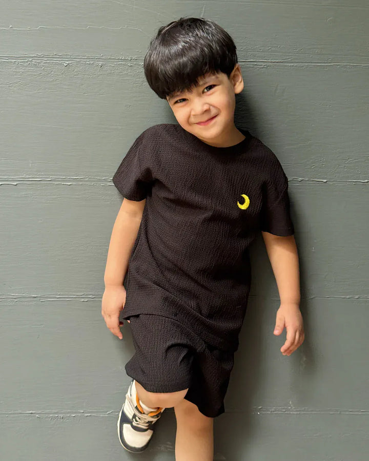 Child wearing a black t-shirt with a yellow logo against a gray wall