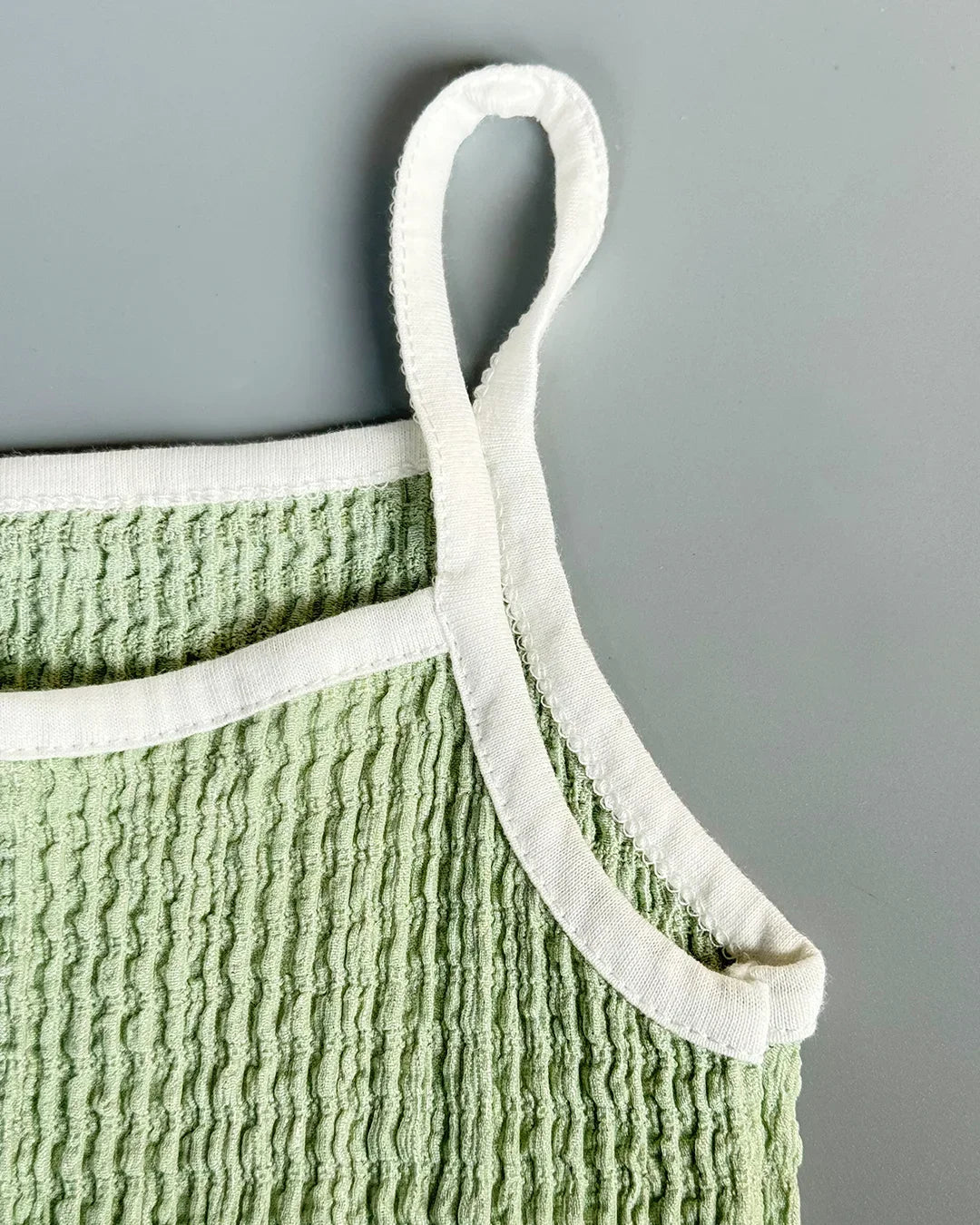 Green textured garment with white trim on a gray background