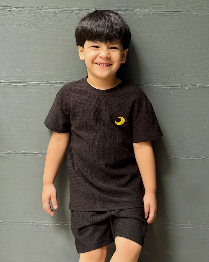 Child wearing a black t-shirt with a yellow logo against a gray wall