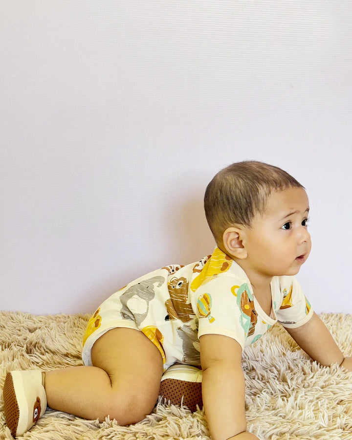 Baby wearing a yellow outfit with animal prints on a beige surface.