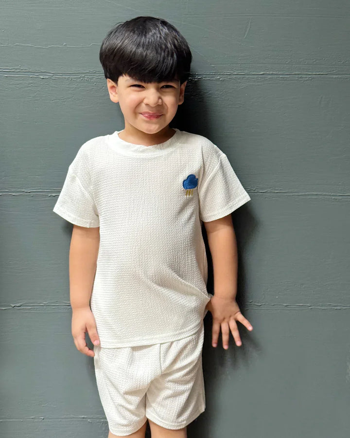 Child wearing a white t-shirt and shorts against a gray wall