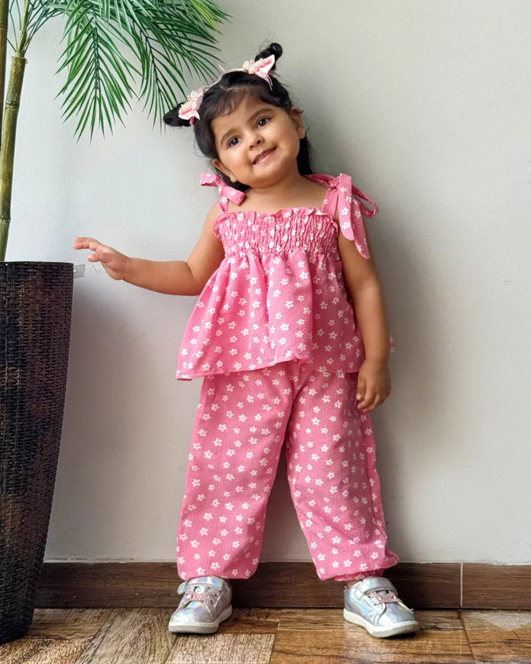 Child wearing a pink outfit with white patterns standing indoors.