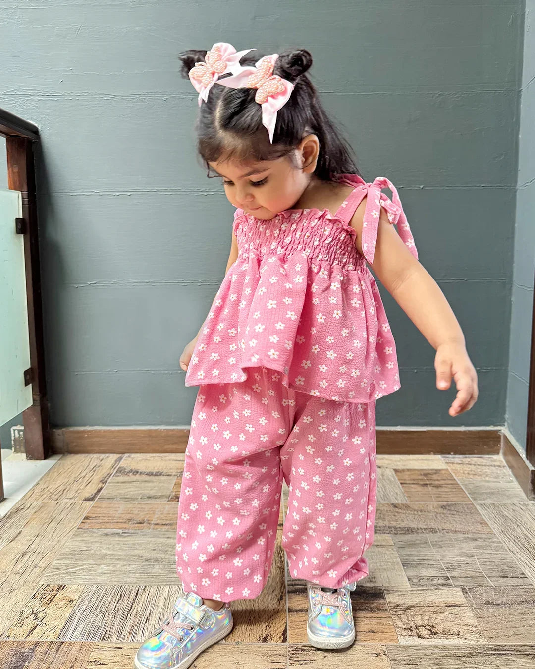 Child wearing a pink outfit with white patterns on a wooden floor.