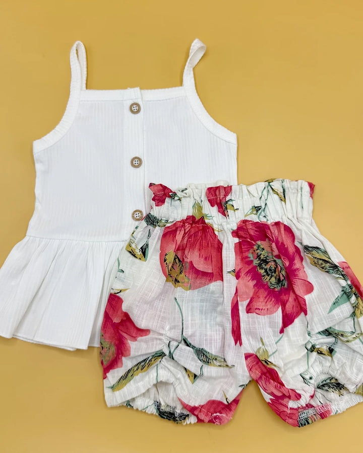 White sleeveless top with buttons and floral shorts on a yellow background