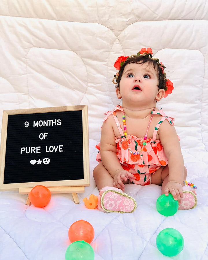 Baby sitting on a white blanket with colorful balls and a sign reading '9 Months of Pure Love'.