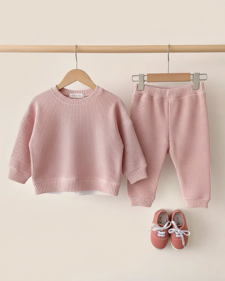 Pink children's sweater and pants set with shoes on a beige background