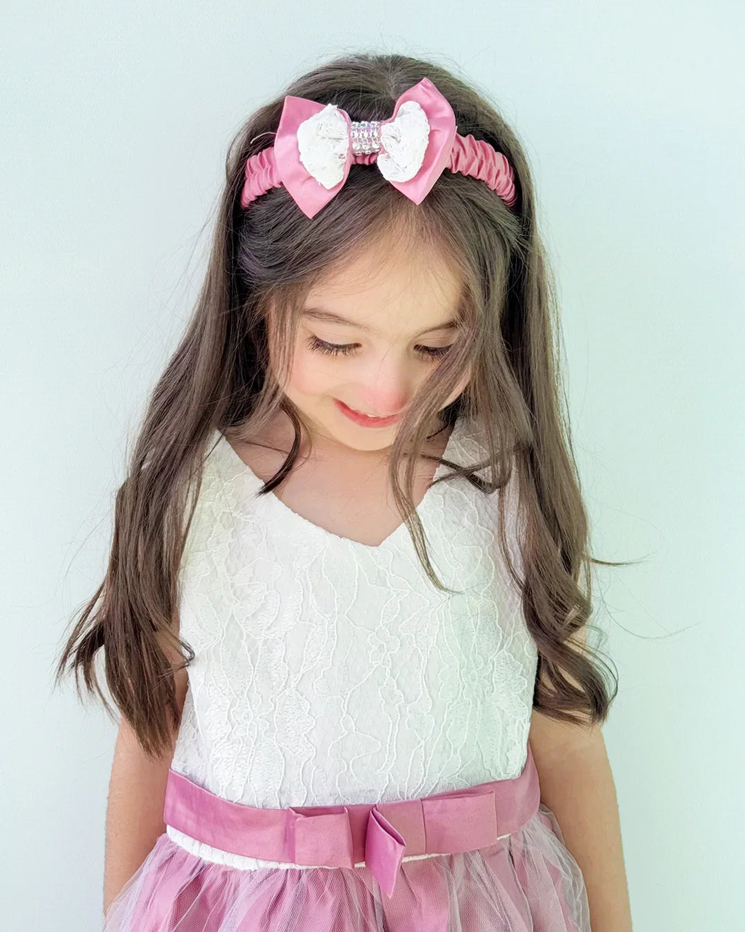 Young girl wearing a white top with pink accents and a matching headband against a light background