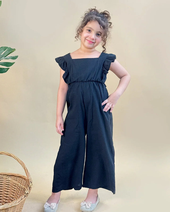 Young girl wearing a black dress with ruffled sleeves against a beige background