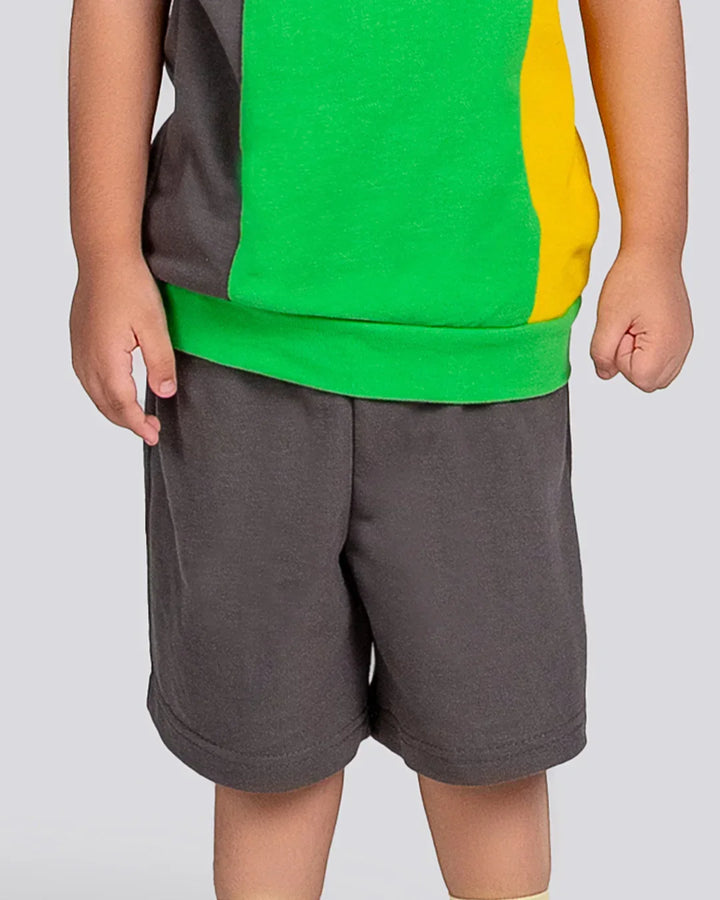 Child wearing a green and yellow shirt with gray shorts on a plain background