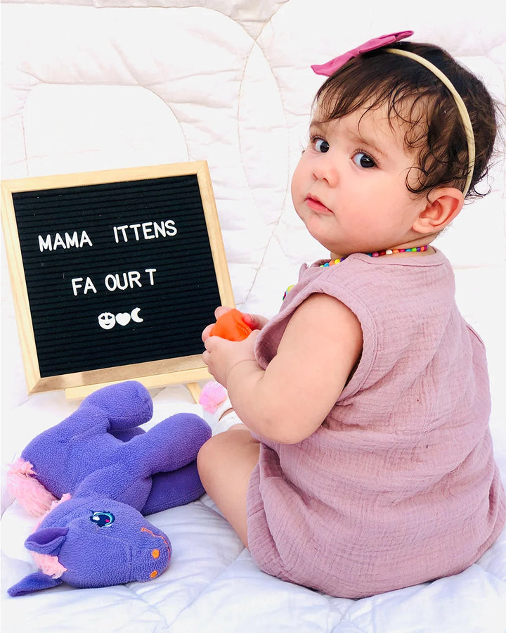 Baby sitting on a bed with toys and a letter board displaying text.