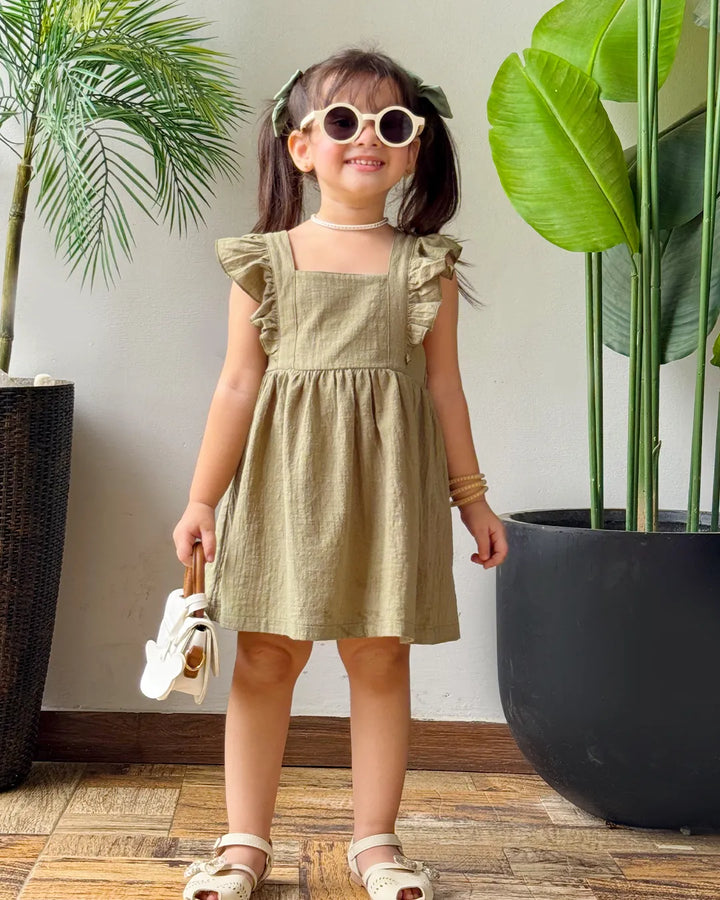 Young girl in a green dress standing indoors with plants around