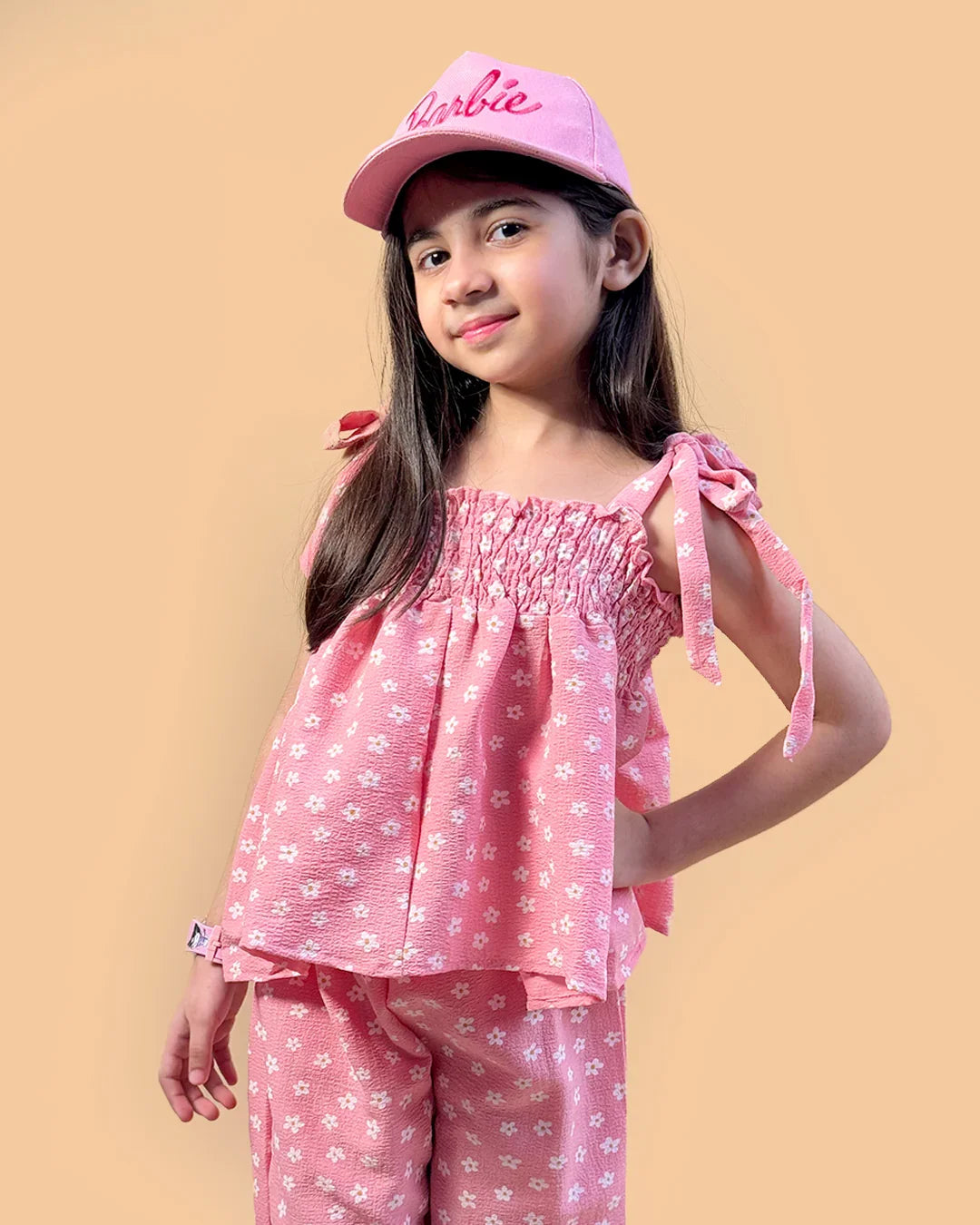 Young girl wearing a pink 'Barbie' cap and matching outfit on a beige background