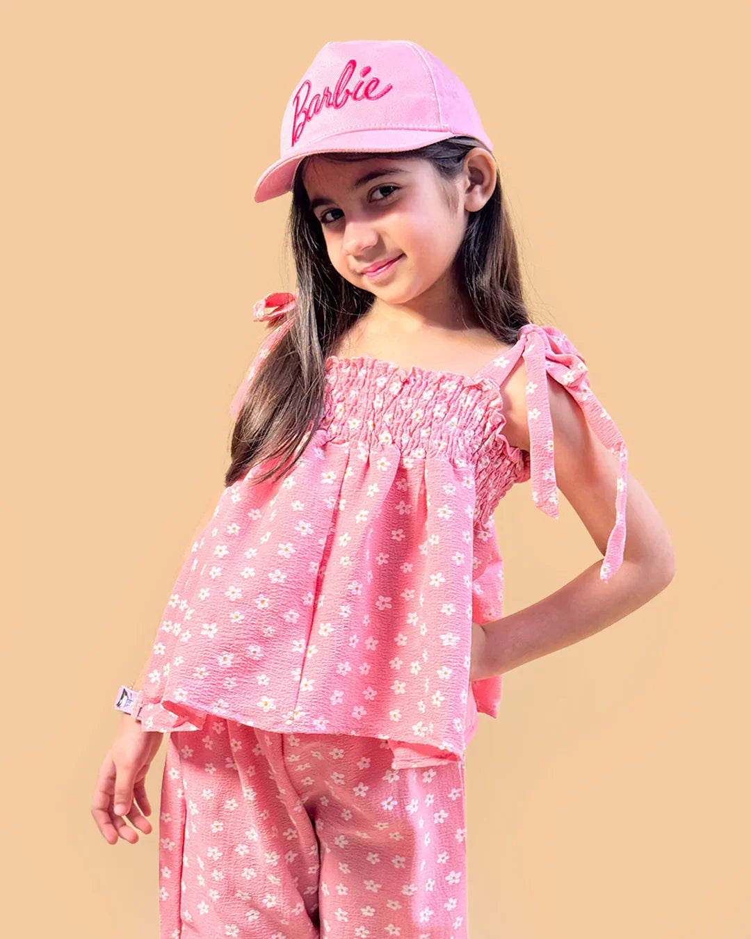 Young girl wearing a pink outfit with a matching cap on a beige background