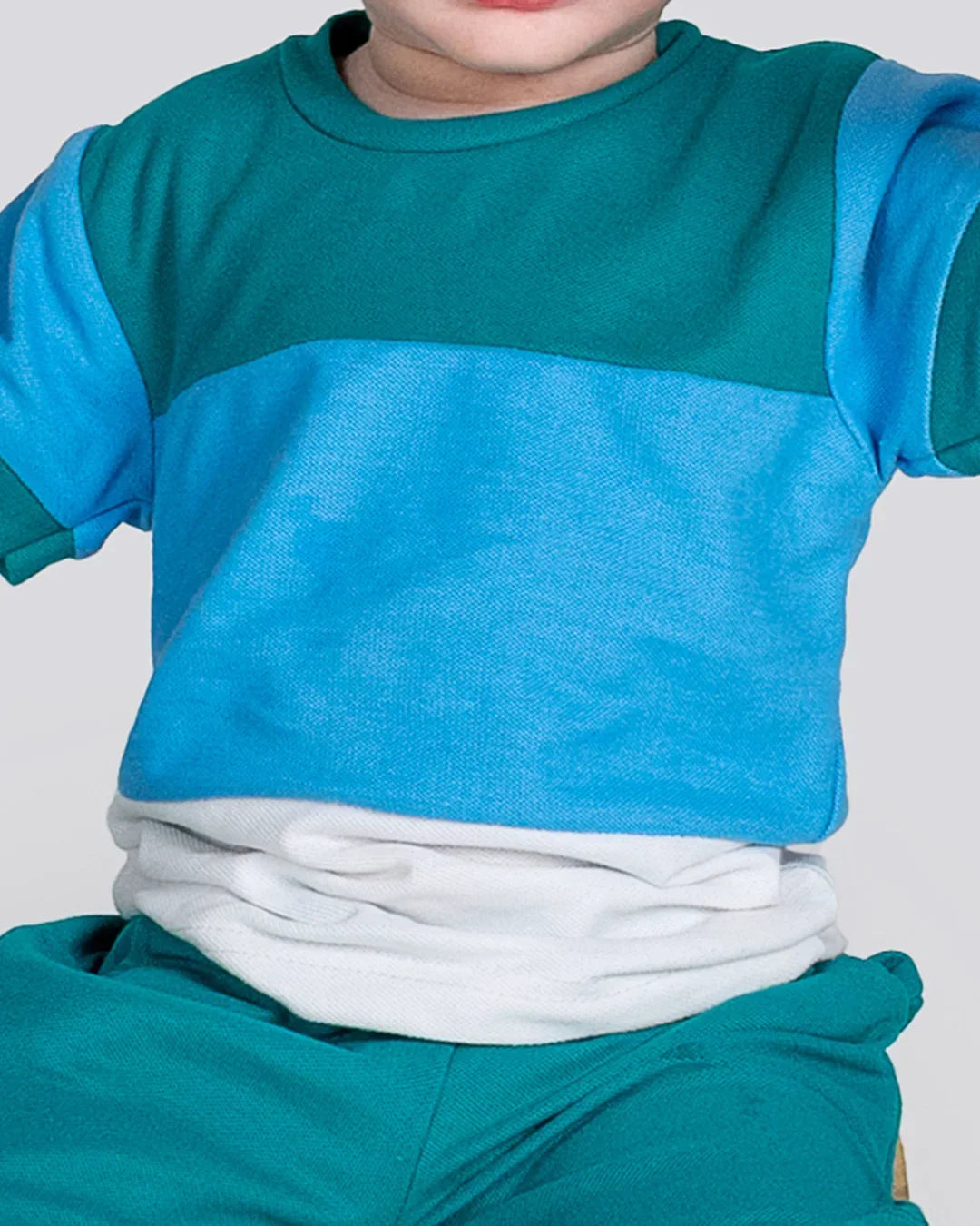 Child wearing a blue and teal outfit with a white shirt underneath on a light gray background