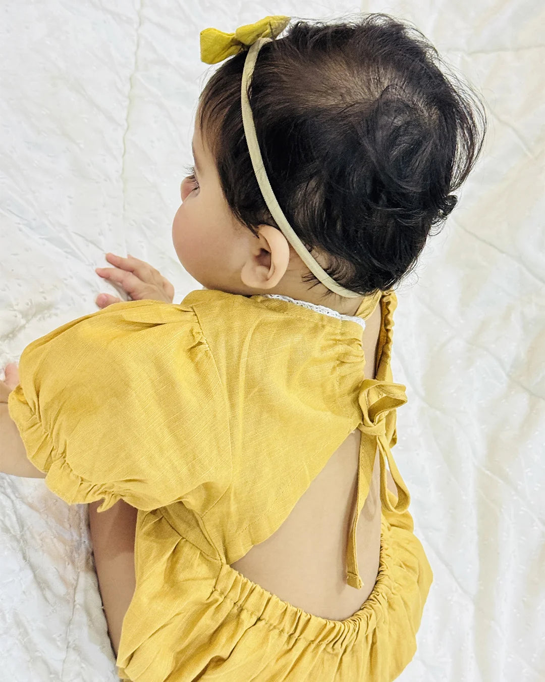 Baby wearing a yellow outfit with a bow on a white blanket