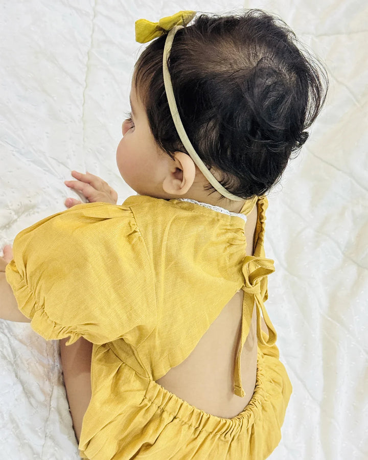 Baby wearing a yellow outfit with a bow on a white blanket