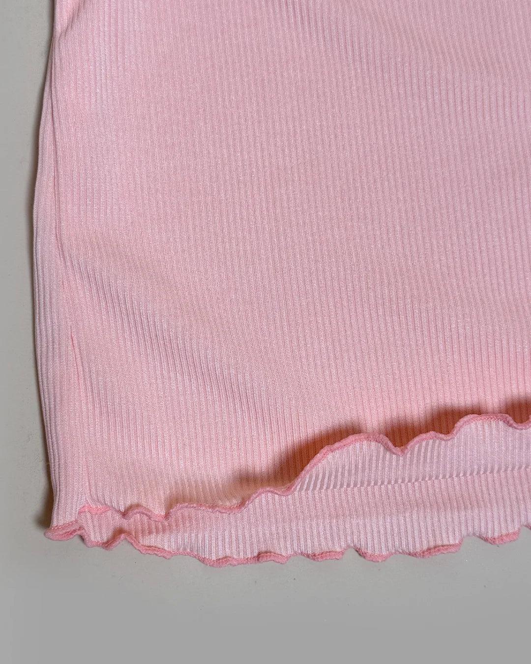 Close-up of a pink ribbed fabric with scalloped edge on a gray background
