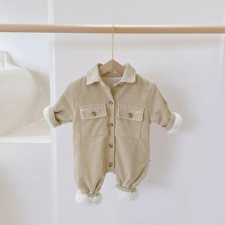 Beige baby romper with white cuffs and buttons on a wooden hanger against a white background